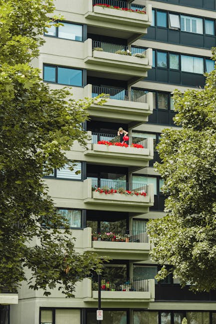 Exterior view of a multi-storey residential building constructed with red brick, featuring large white-framed sash windows and black wrought iron balconies. The building's façade is clean and well-ma